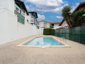 A swimming pool with a metal ladder, surrounded by a white wall and a green fence.