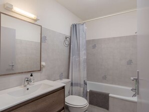 A bathroom with a toilet, sink, mirror, shower curtain, and bathtub.