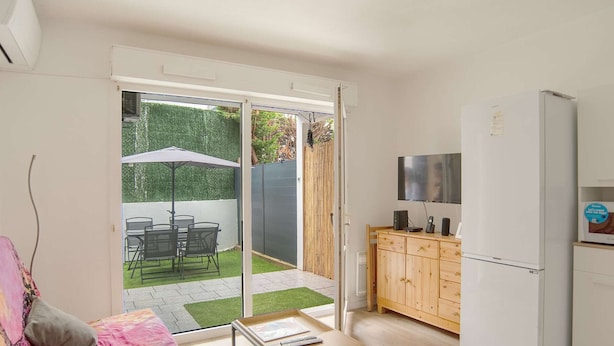 A modern apartment with a kitchen, a dining area with a table and chairs, a sofa, and a sliding glass door leading to a garden. - Renovated apartment in Hendaye with air conditioning and parking (Hendaye)