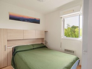A bedroom with a bed, a headboard, a window, and a painting on the wall.