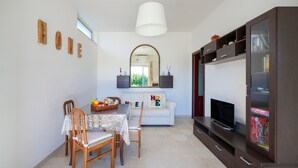 A dining area with a table, chairs, a fruit basket, a sofa, a TV, and a cabinet. - Apartment 'La Campanella' with Shared Terrace, Wi-Fi and Air Conditioning (putignano)