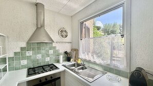 A compact kitchen with a gas stove, oven, and a window with a view of greenery.