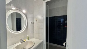 A bathroom with a white sink, a round mirror, and a shower area.