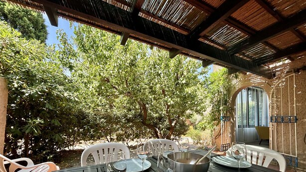 An outdoor dining area with a table set for four, surrounded by trees and a covered patio.