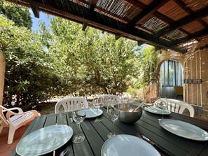 An outdoor dining area with a table set for four, surrounded by trees and a covered patio. - 3-room apartment with terrace near the beach in Lumio (Lumio)