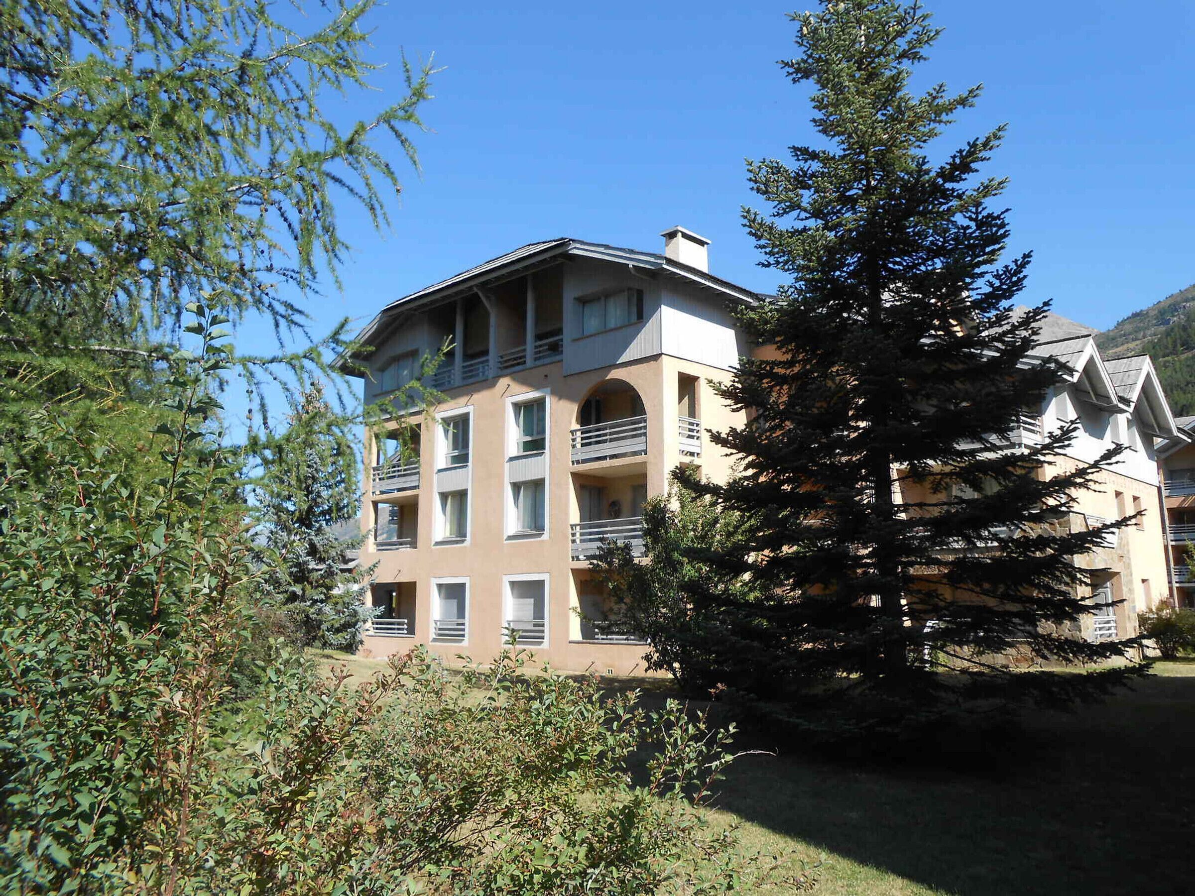 Un hôtel à plusieurs étages, doté de balcons, entouré d’arbres et adossé à un paysage montagneux.