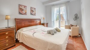Una camera da letto con un letto di legno, un comodino, una lampada, una sedia e una ventola.
