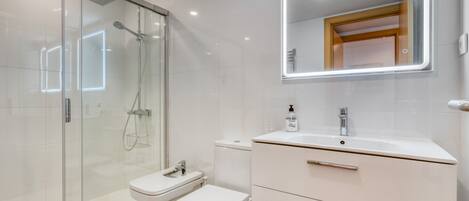 A modern bathroom with a glass-enclosed shower, a white toilet, and a vanity with a mirror.