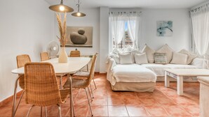 Un soggiorno moderno con zona pranzo, pareti bianche e un'ampia finestra con tende.