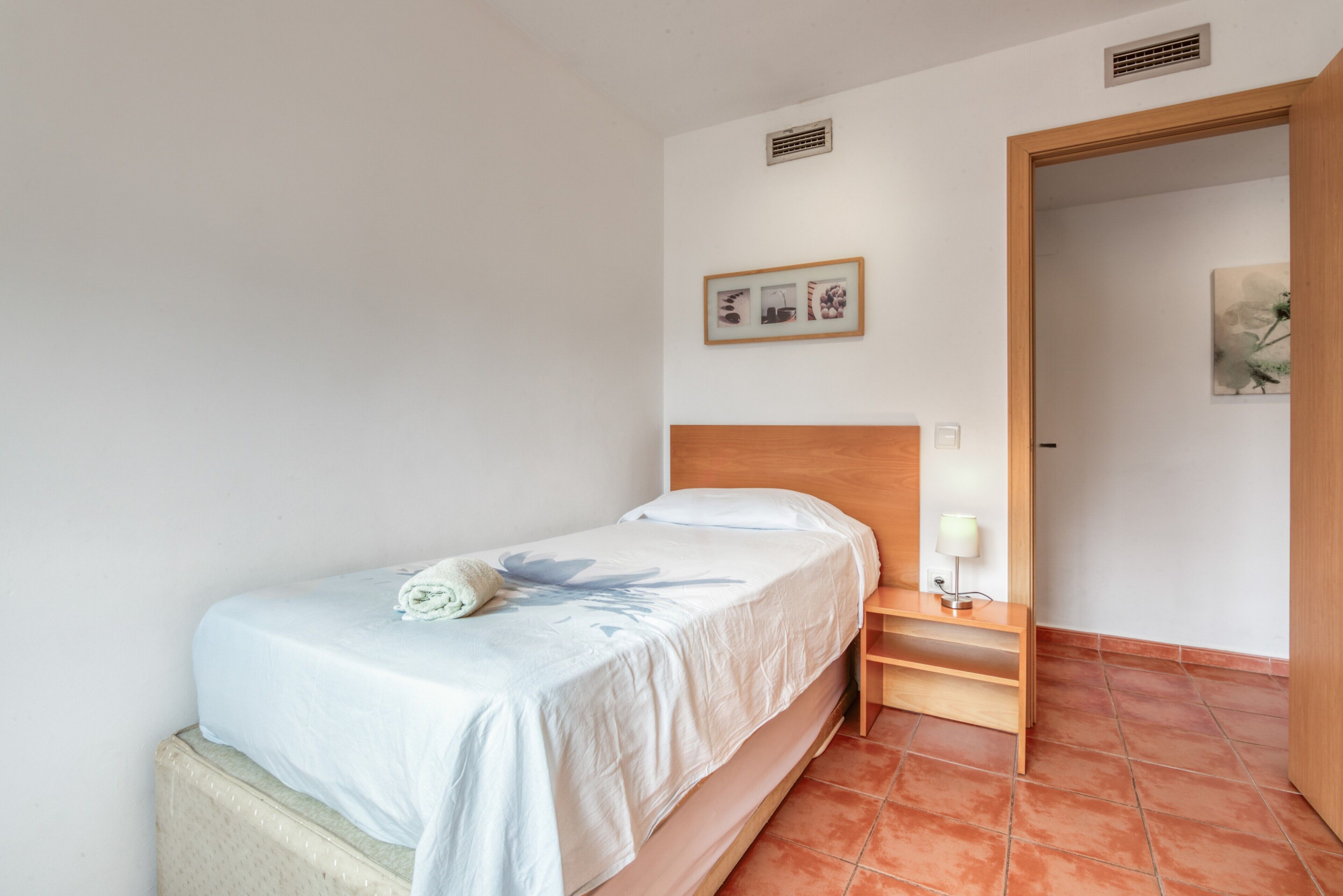 A bedroom with a bed, bedside table, lamp, and a picture on the wall.