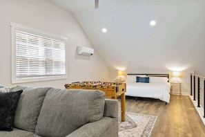 A cozy loft bedroom with a bed, a sofa, and a foosball table.