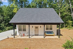 A small, single-story cabin with a covered porch, a door, and a seating area with a sofa and chairs.
