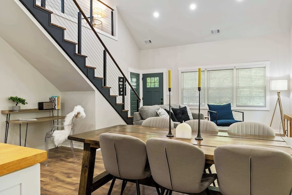 A modern living room with a dining area, a staircase, and a view of the outdoors.