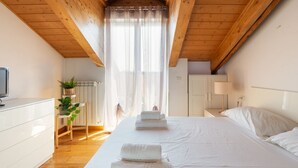 A bedroom with a wooden ceiling, a bed with white linens, a bedside table with a lamp, and a radiator.