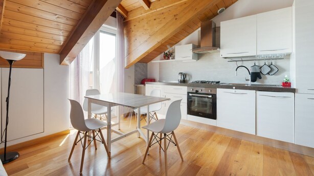 A modern kitchen with white cabinets, a dining table with chairs, and a wooden ceiling.
