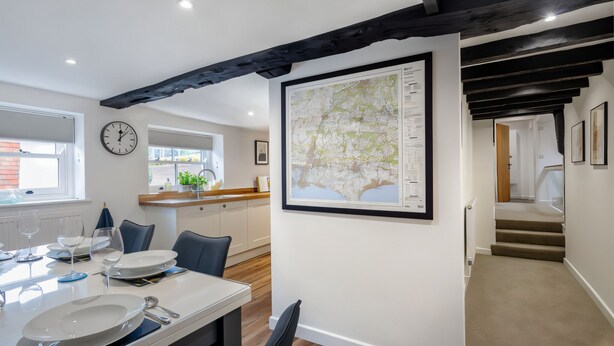 A dining area with a white table set for two, a clock on the wall, and a framed map. - Stylish 16th century apartment in Petersfield town centre (Petersfield)