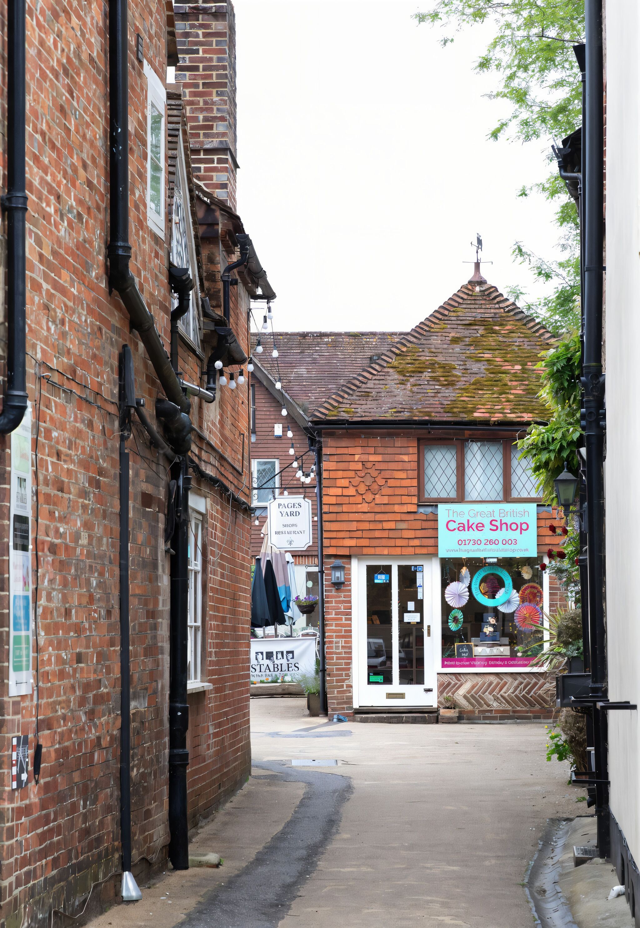 A narrow street with a brick building on the left and a shop named "The Great British Cake Shop" on the right.