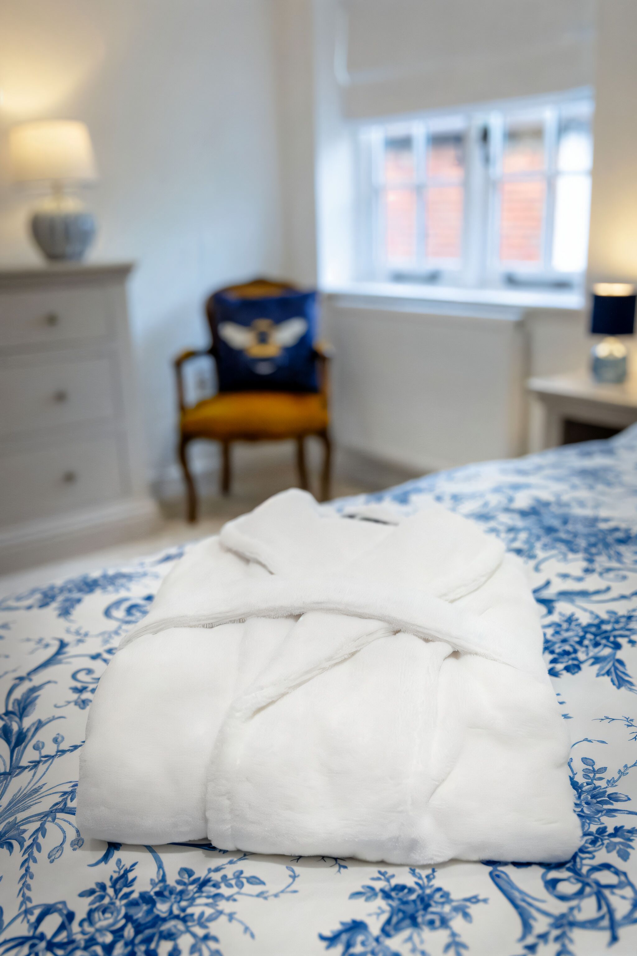 A neatly made bed with a blue floral bedspread, a white pillow, and a folded white robe on the bed.