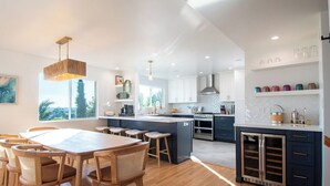 A modern kitchen with a central island, wooden dining table, and bar stools.