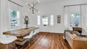 Une pièce spacieuse avec une table à manger en bois, des chaises blanches, un canapé et un lustre.