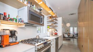 Eine moderne Küche mit Gasherd, Backofen und Mikrowelle. Über der Arbeitsplatte befinden sich Regale mit verschiedenen Küchenutensilien.