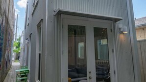 Ein modernes, zweistöckiges Gebäude mit einer großen Glasdoor und Fenstern, einem Deck mit Gartenmöbeln und einem schmalen Gang.