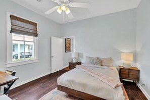 A bedroom with a bed, bedside tables, a ceiling fan, a window with blinds, and a door.