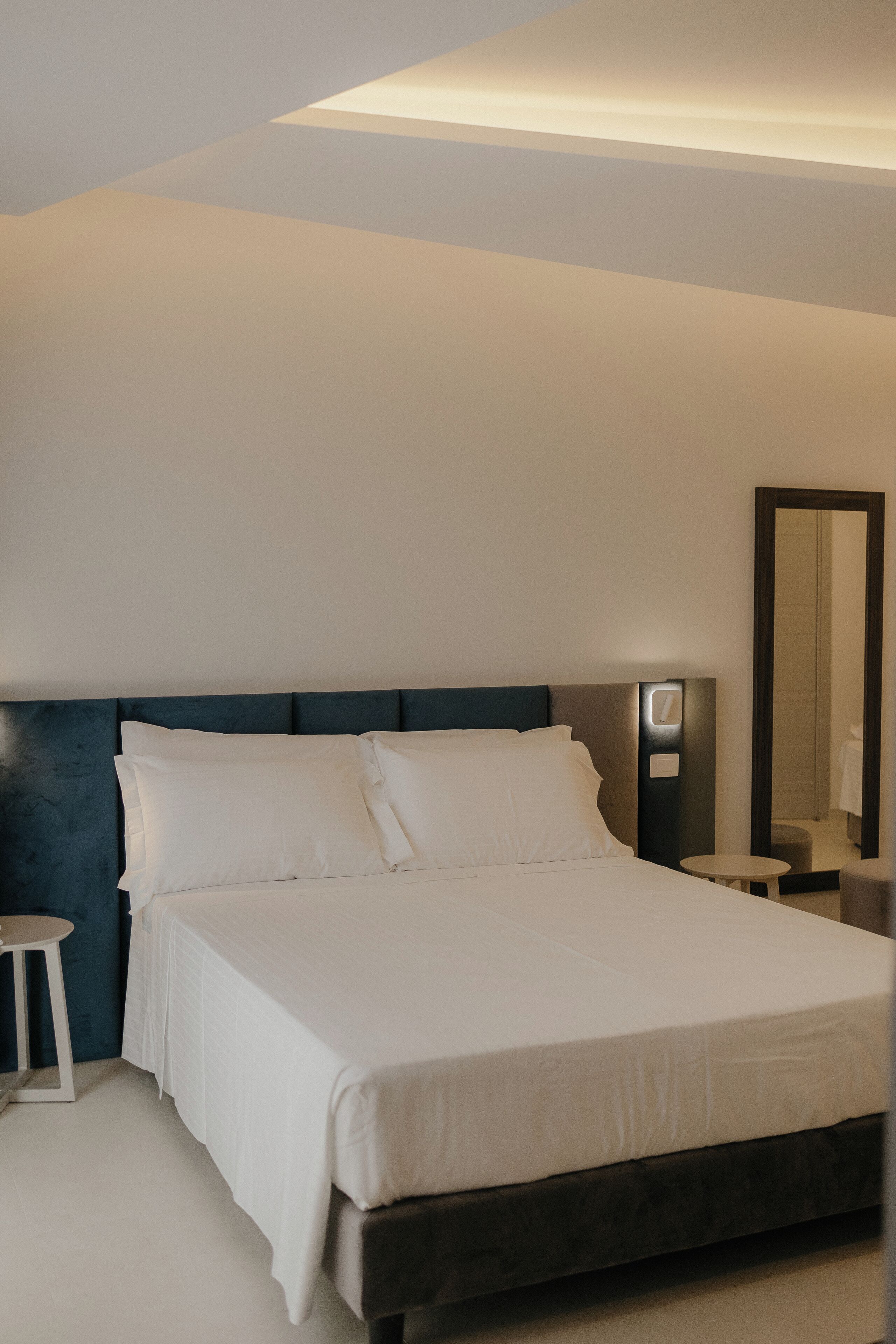 Quarto de hotel moderno com uma cama grande, mesa de cabeceira e espelho.