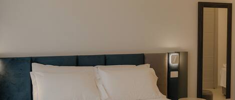 A modern hotel room with a large bed, a bedside table, a nightstand, and a mirror.