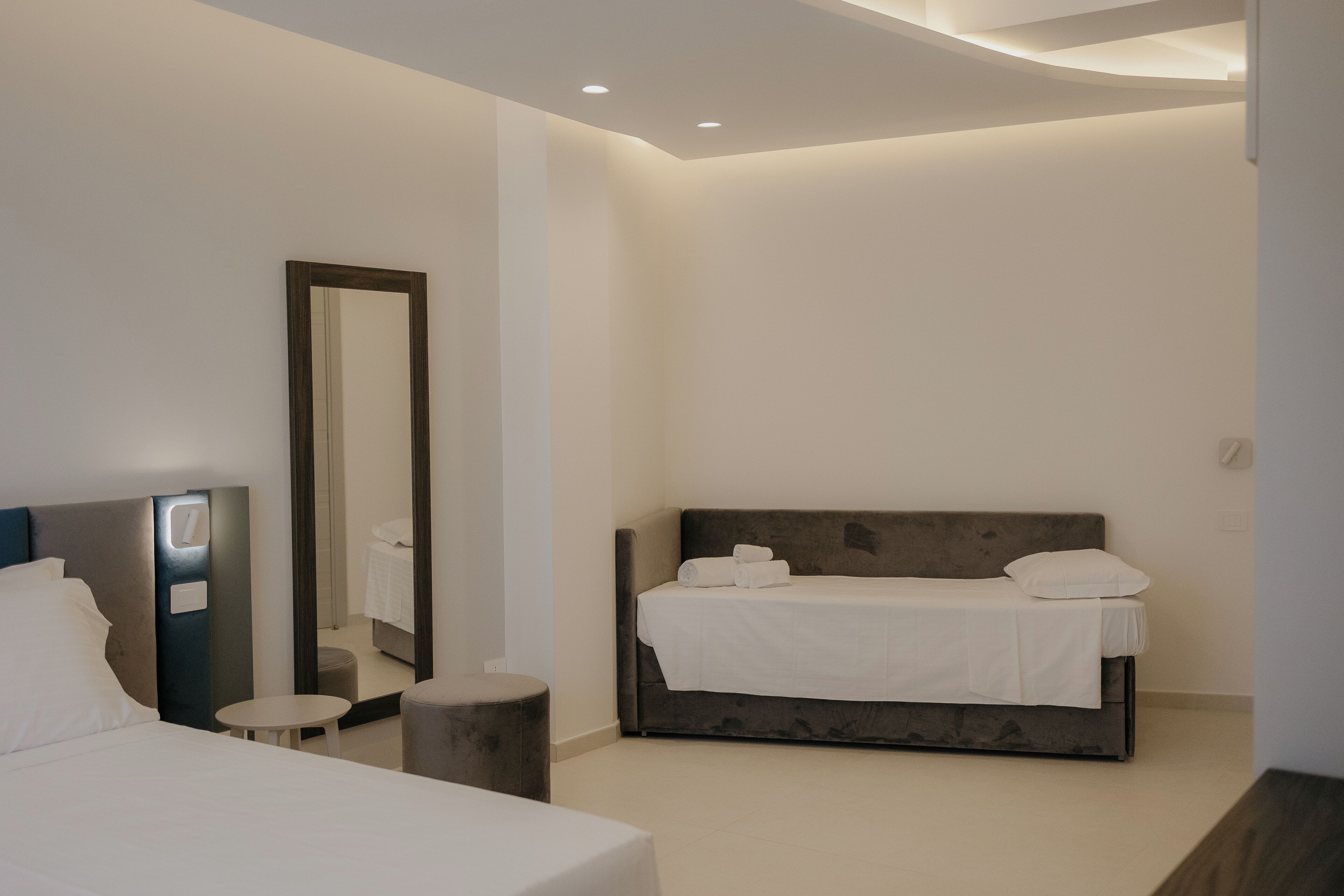 Habitación de hotel moderna con una cama grande, una mesita redonda, un taburete pequeño y un espejo amplio.