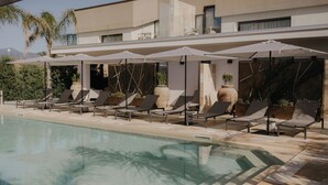 Un espace aménagé au bord de la piscine, avec des chaises longues et des parasols, une piscine à eau claire et un bâtiment moderne en arrière-plan.