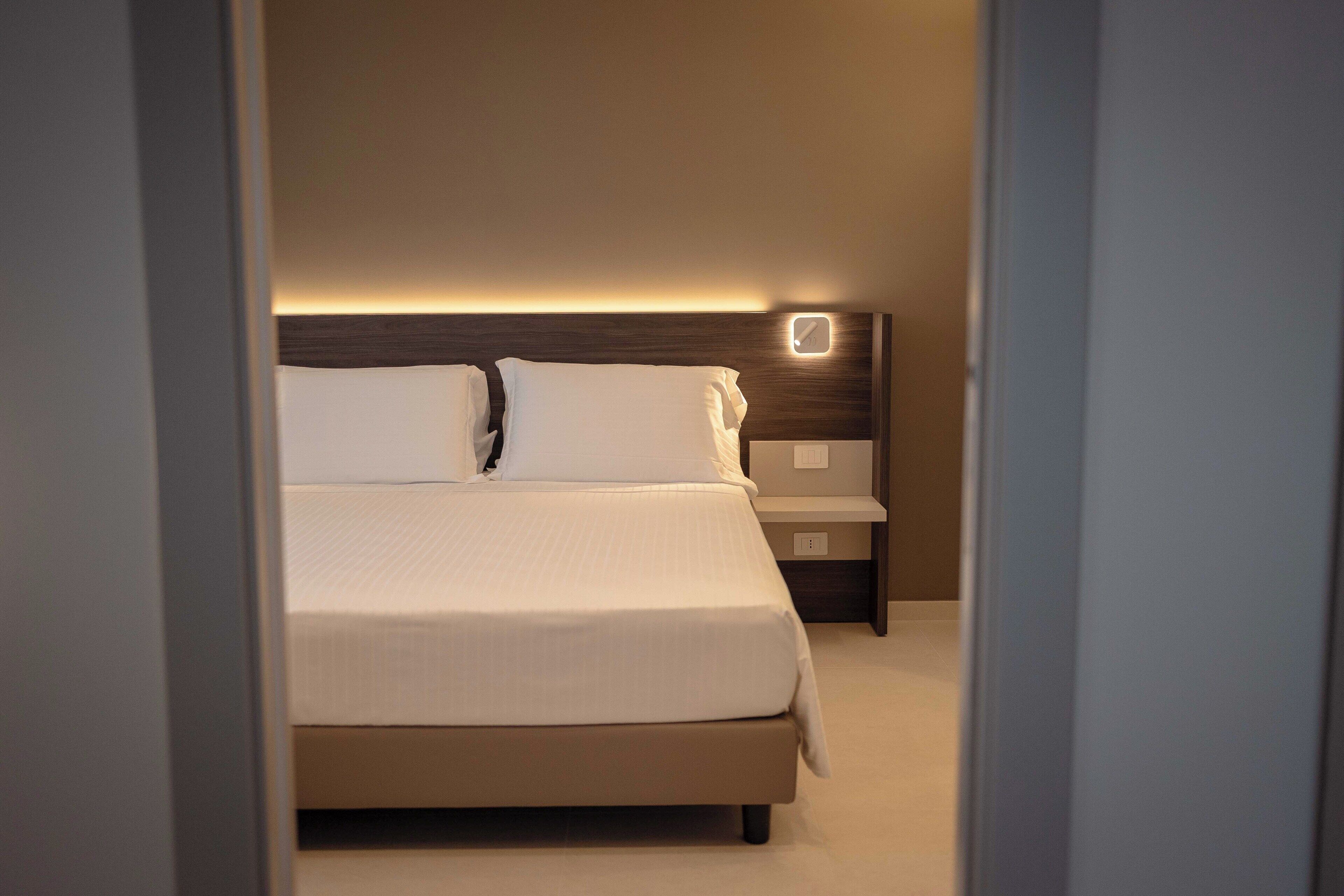 Un lit bien fait, avec une tête de lit, une table de chevet et un luminaire fixé au mur.