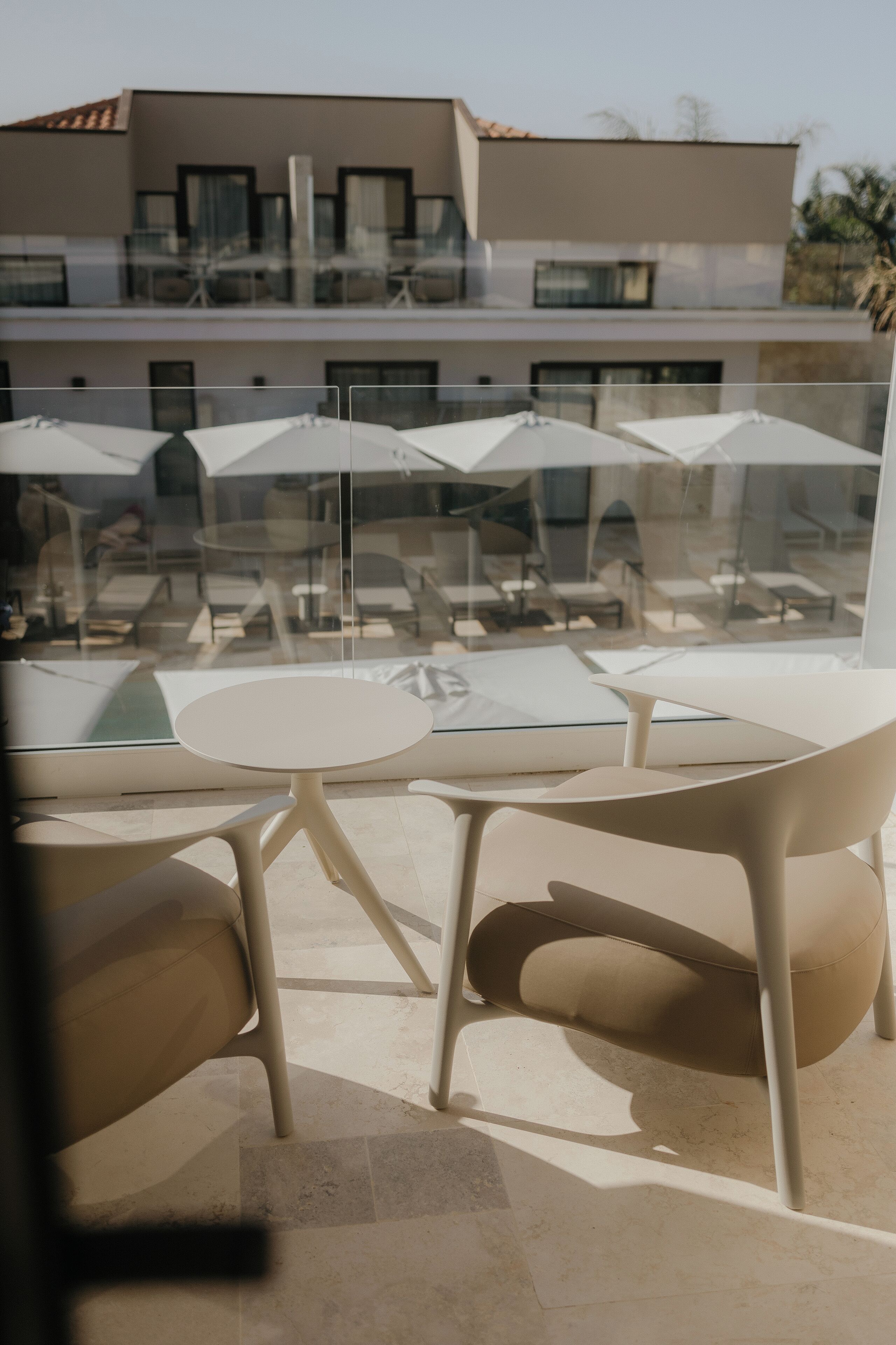 A modern outdoor seating area with a glass balustrade, white tables, and beige chairs.