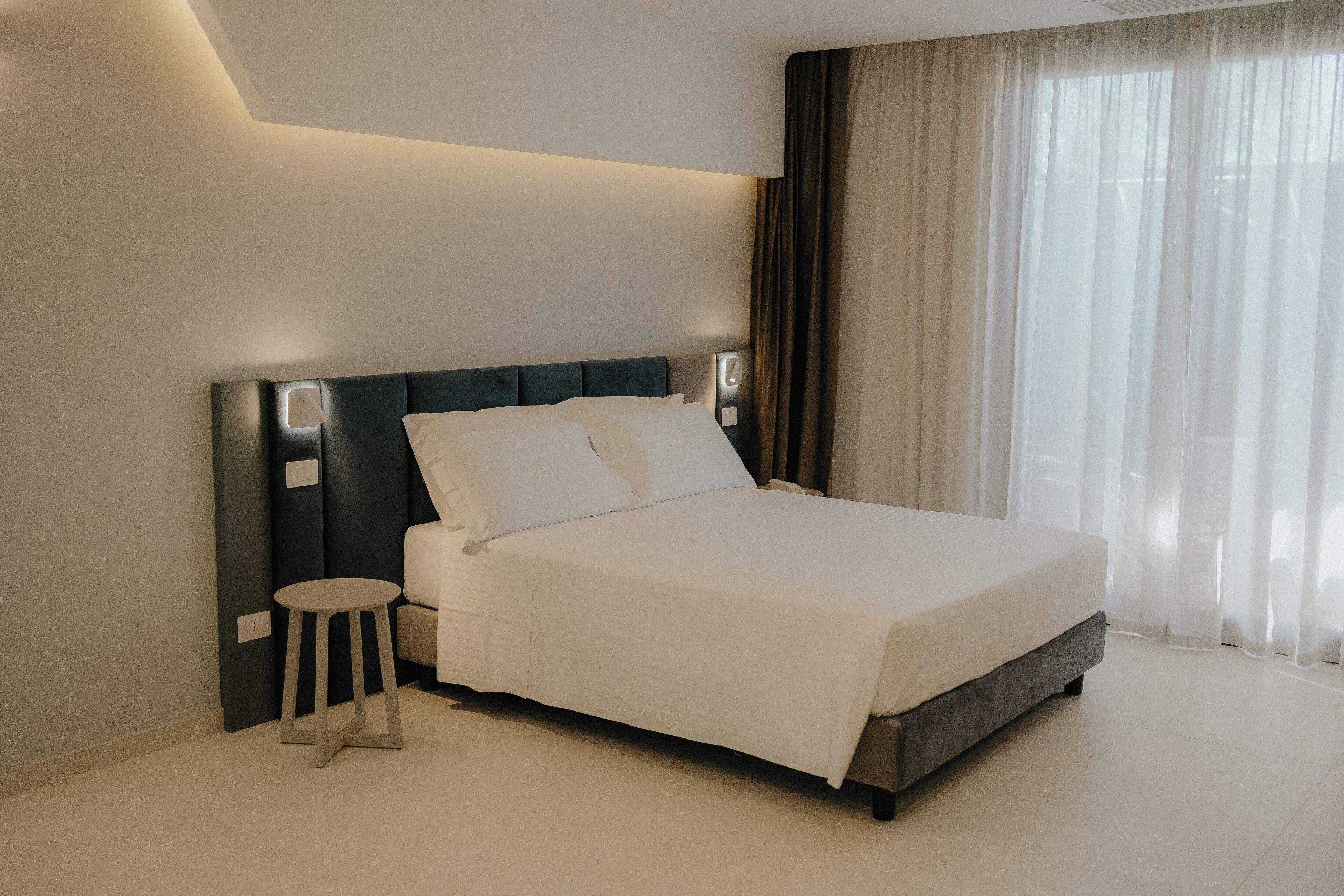A modern bedroom with a large bed, bedside tables, and a small stool.
