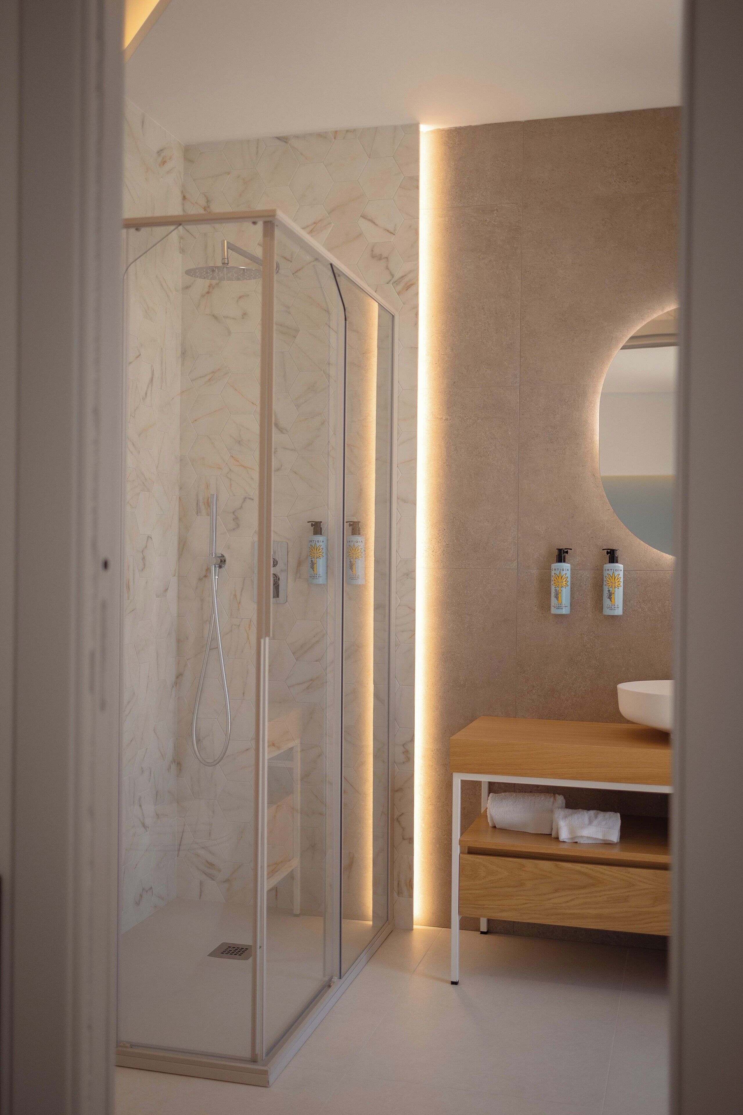 A modern bathroom with a glass-enclosed shower, a wooden vanity, and a marble wall.