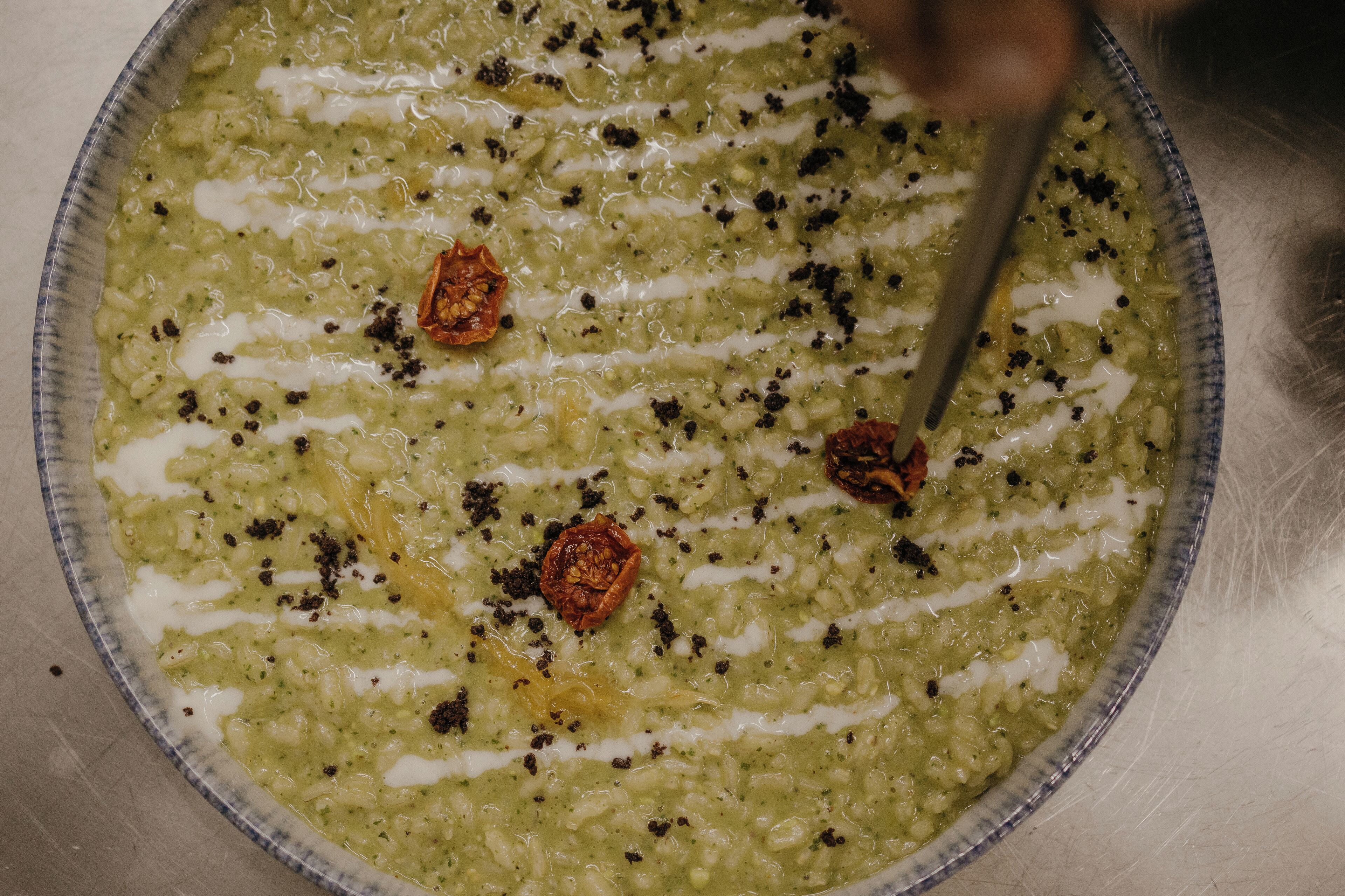A bowl of green soup with black pepper and sun-dried tomatoes.