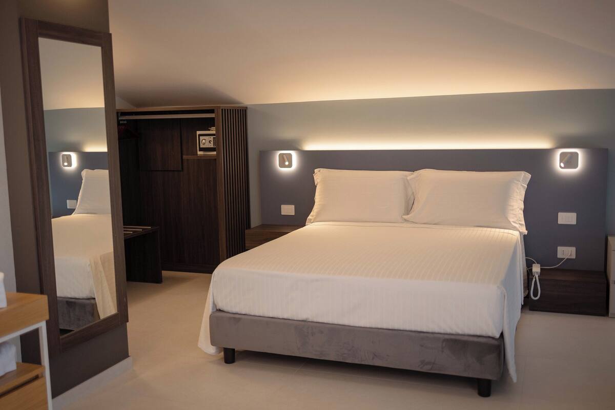 A modern bedroom with a large bed, bedside tables, a mirror, and a built-in wardrobe.
