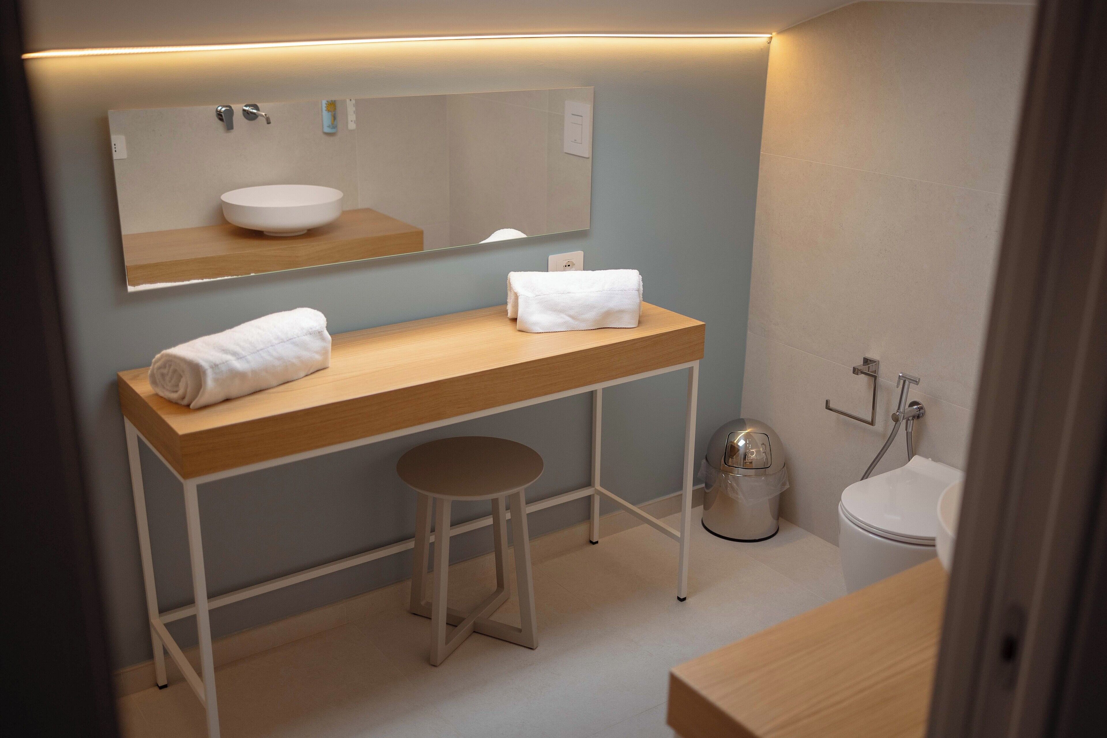A modern bathroom with a wooden vanity, a round sink, a mirror, a toilet, and a trash can.