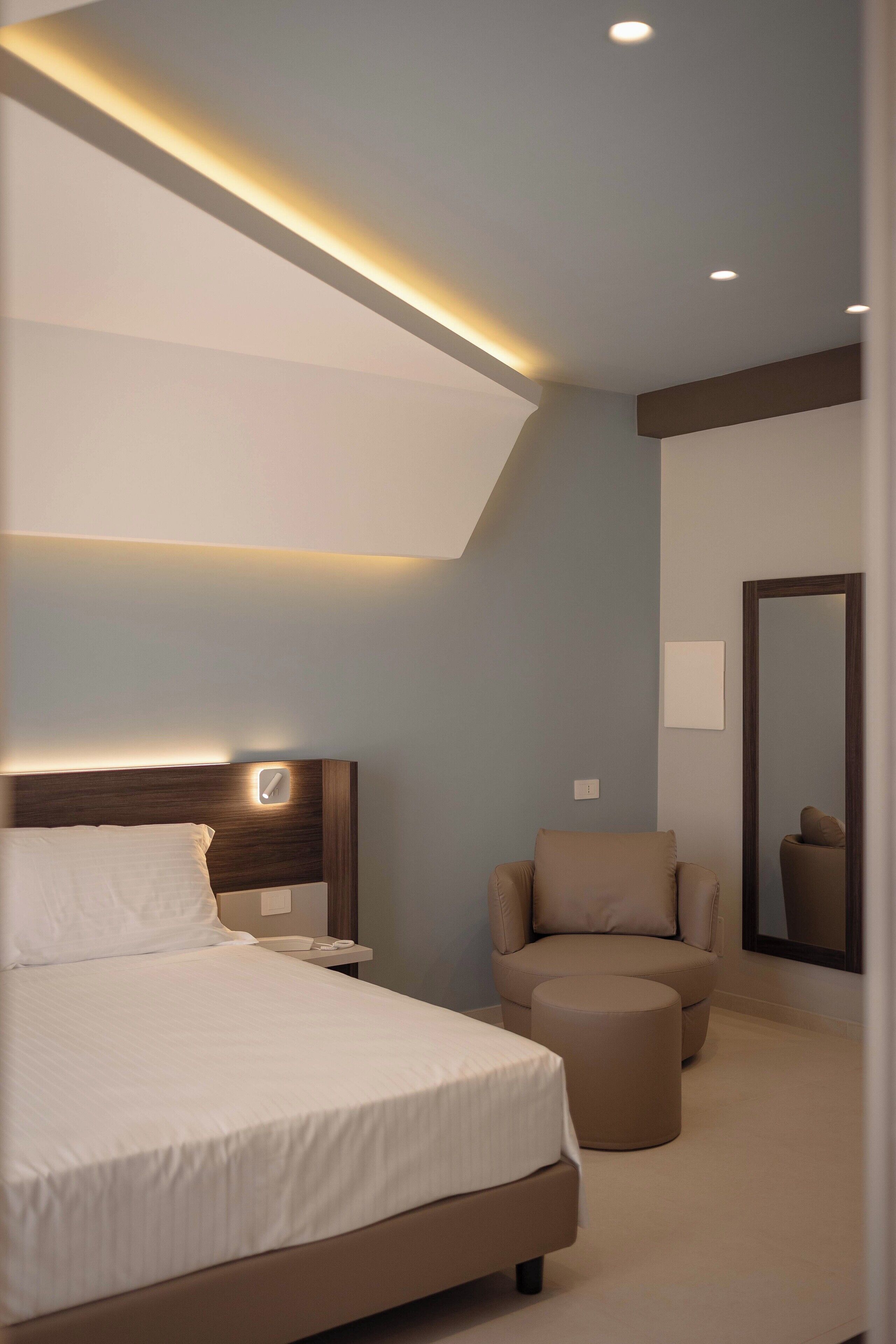 A modern bedroom with a large bed, a bedside table, a chair, and a mirror on the wall.