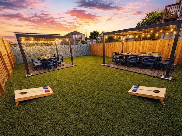 An outdoor patio with a wooden deck, string lights, and a table set for dining.