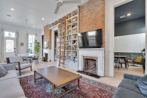 Un salon spacieux avec une cheminée, une bibliothèque, un téléviseur et un coin repas.