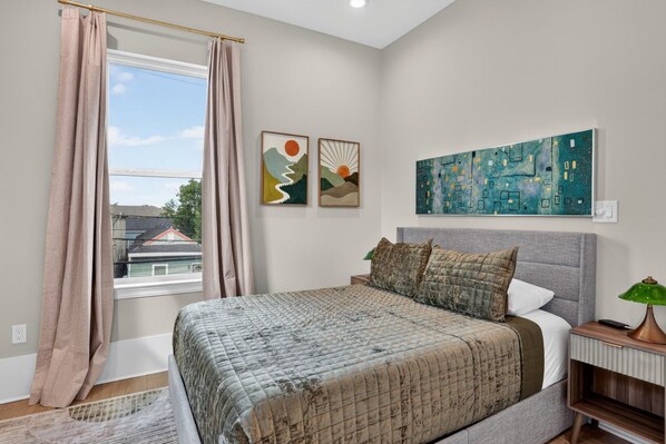 Une chambre à coucher avec un lit, une table de chevet, une lampe et des œuvres d’art accrochées au mur.