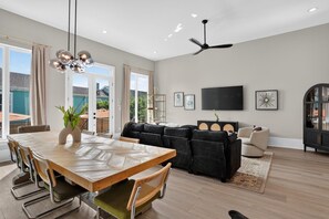 Un salon moderne comprenant un coin repas, un canapé noir, un téléviseur à écran plat et un ventilateur de plafond.