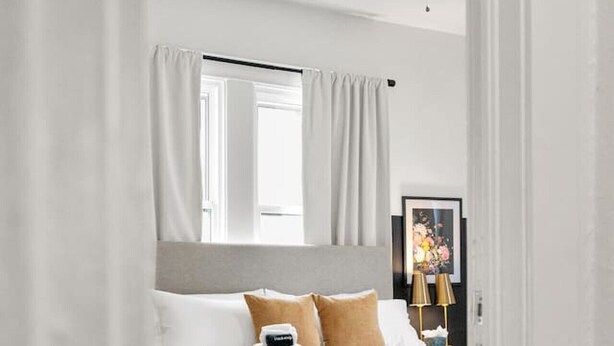 A modern bedroom with a bed, white curtains, a ceiling fan, and a framed picture on the wall.