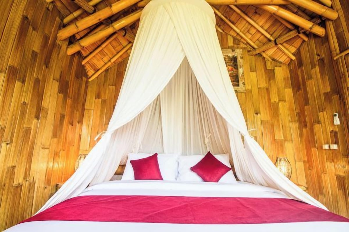 Una cama con dosel, ropa de cama blanca y almohadas rojas en una habitación con piso de bambú.