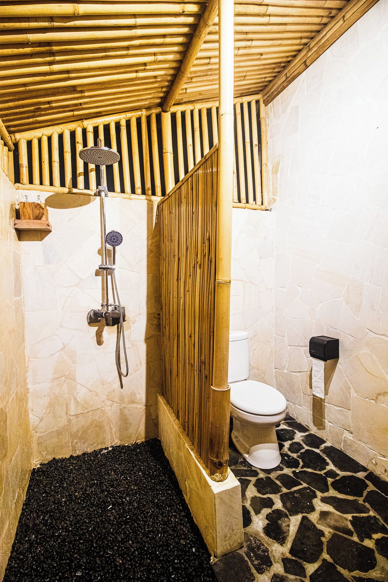A shower with a bamboo ceiling, a stone floor, and a toilet with a stone wall.
