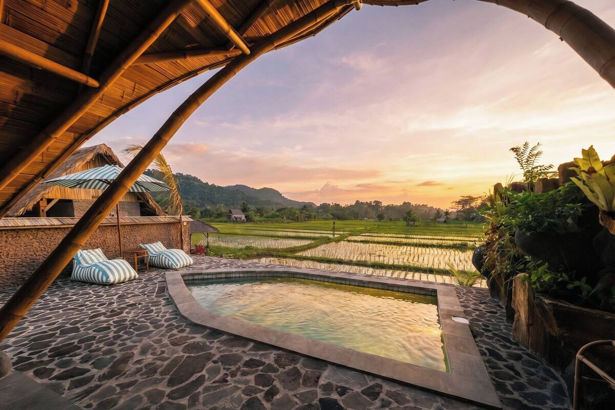 A stone pool with a view of rice fields and a thatched-roof structure.