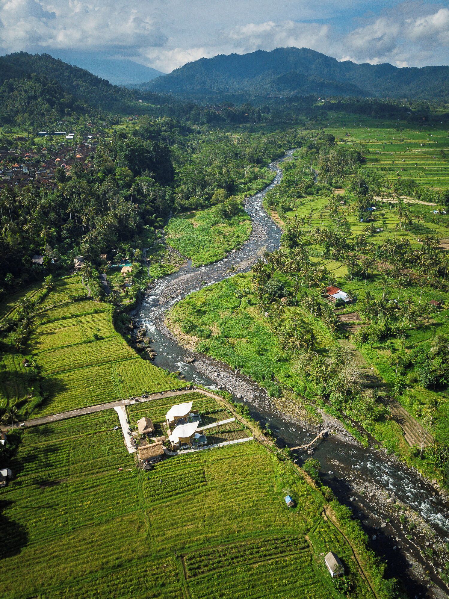Vista aérea de un paisaje rural con campos en terrazas, un río y casas dispersas.