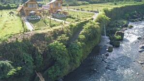 Et træhus med balkon, omgivet af frodig vegetation og en flod.