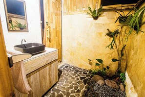 A bathroom with a stone floor, a wooden cabinet, a black sink, and green plants. - Uma D Mapad Sidemen (Sidemen)